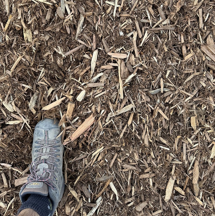Close-up view of mulch, with jagged, textured pieces scattered across the ground. The earthy brown wood chips are commonly used in Calgary landscaping supplies for moisture retention, weed control, and soil health.
