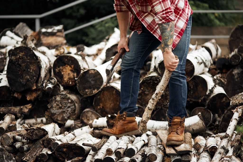 Man stacking birch firewood outdoors in Calgary, holding an axe and preparing logs for home heating during winter