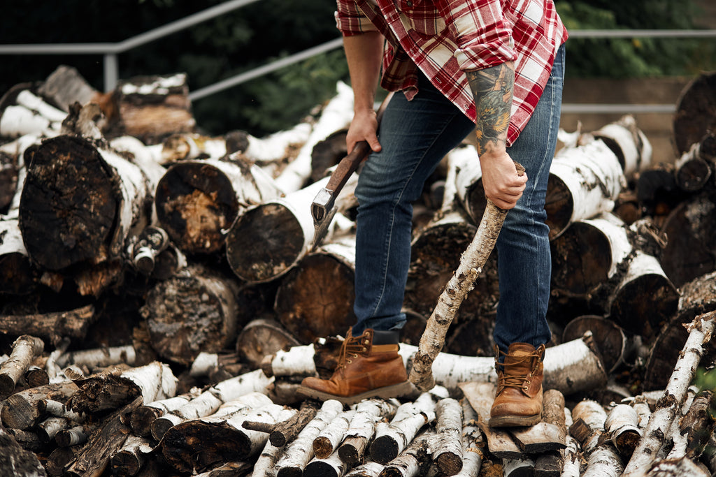 Man stacking birch firewood outdoors in Calgary, holding an axe and preparing logs for home heating during winter